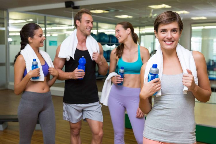 Fit woman smiling at camera in busy fitness studio at the gym